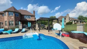 Luxury backyard with an in-ground pool, slide, basketball hoop, lounge chairs, and a pergola near a brick home.