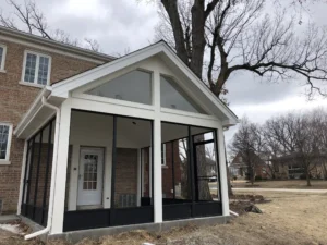 Screened-in porch with a gable roof attached to a brick house.