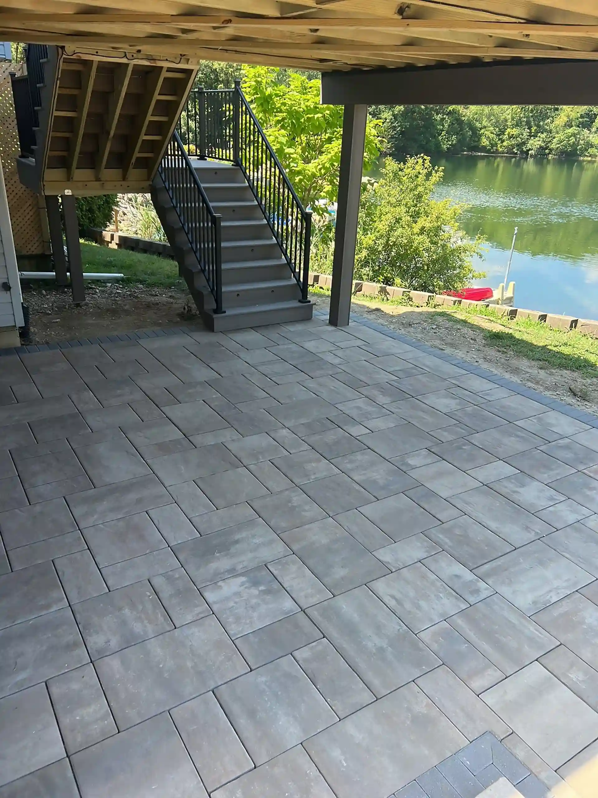 modern patio with gray pavers, stairs to the elevated deck, and lake view