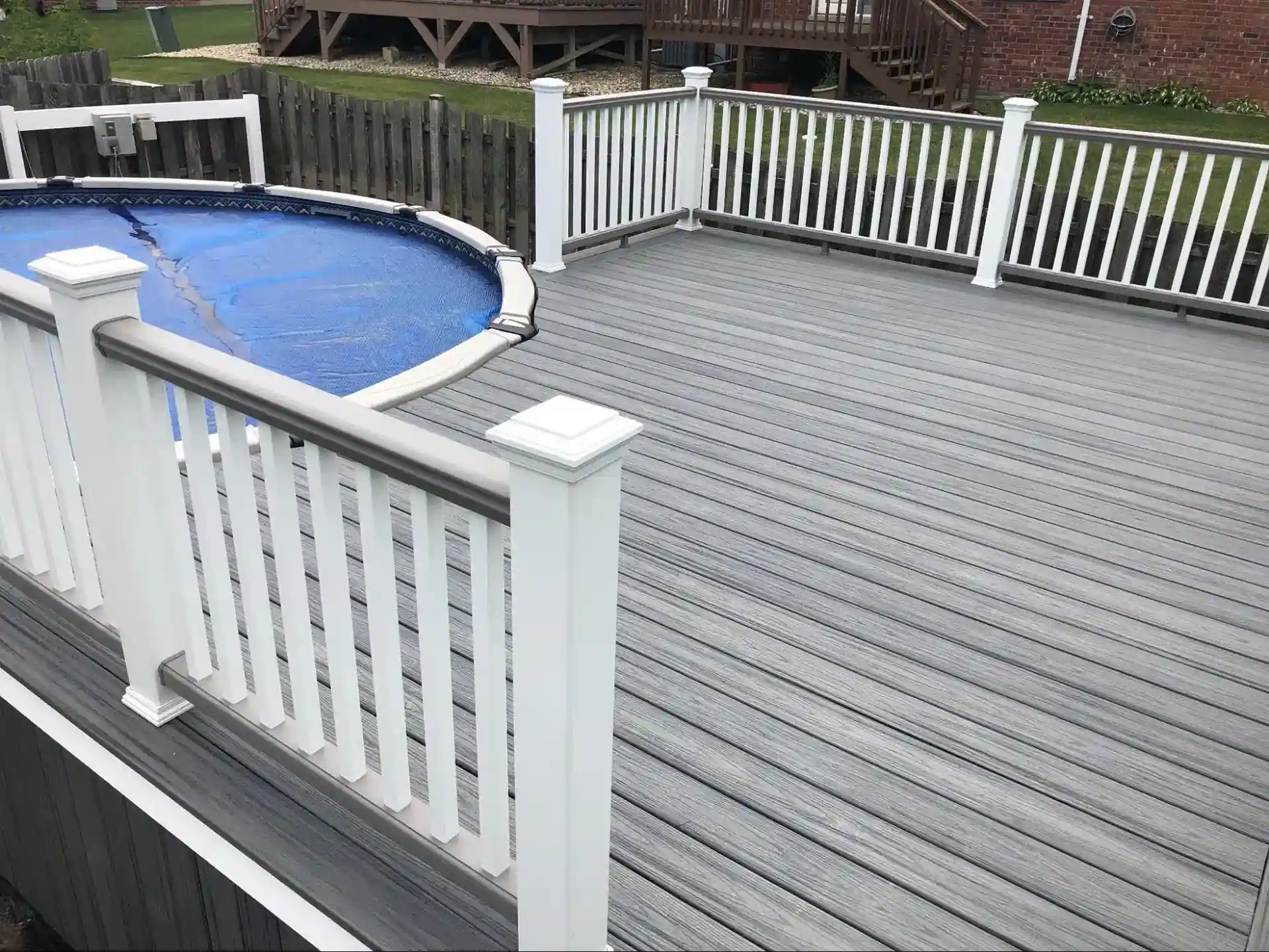 gray composite pool deck with white railings surrounding an above-ground pool with a cover