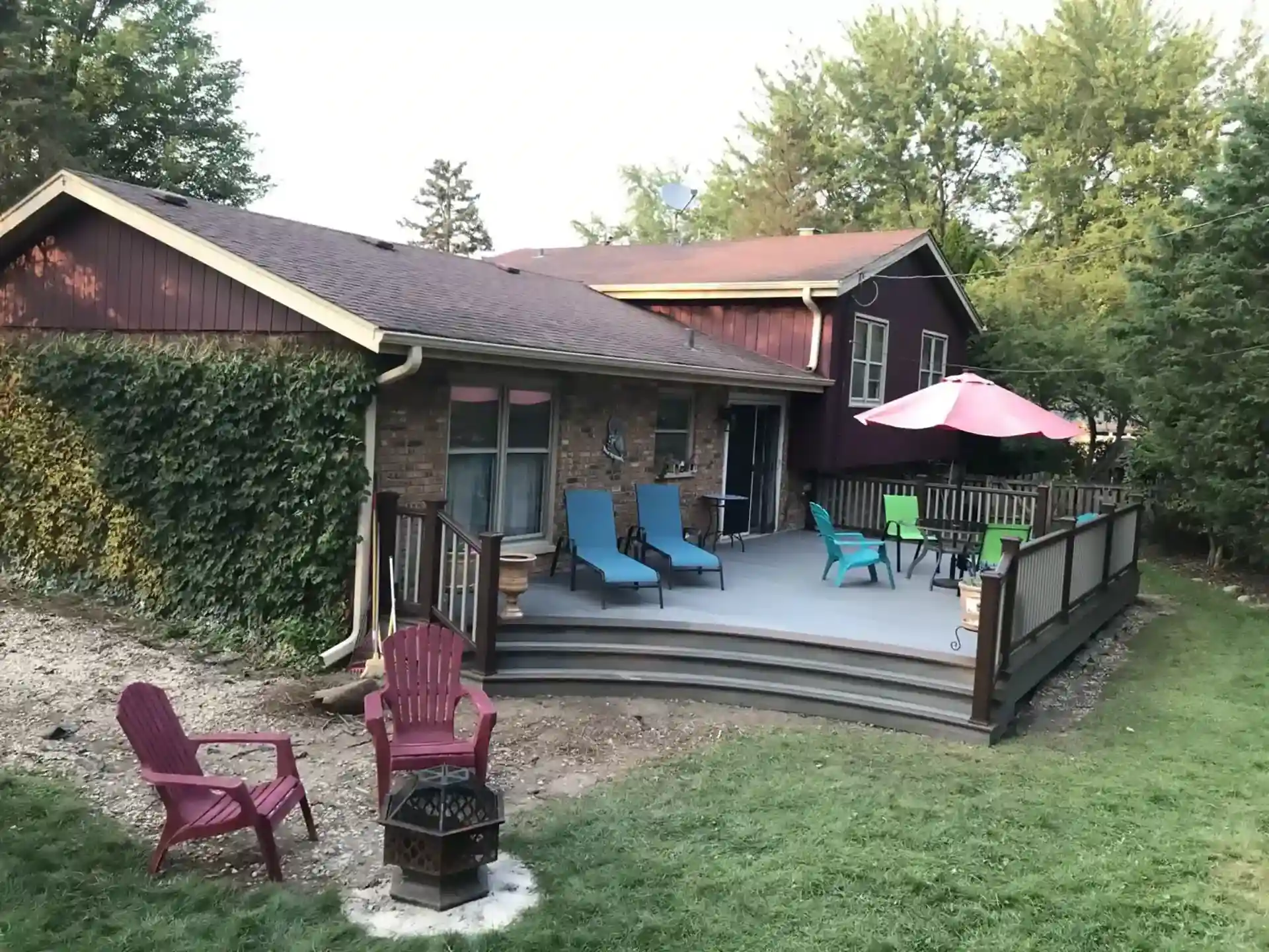 custom deck with a mix of comfortable seating, including lounge chairs and colorful patio furniture, surrounded by a wooden railing and lush greenery in the background.