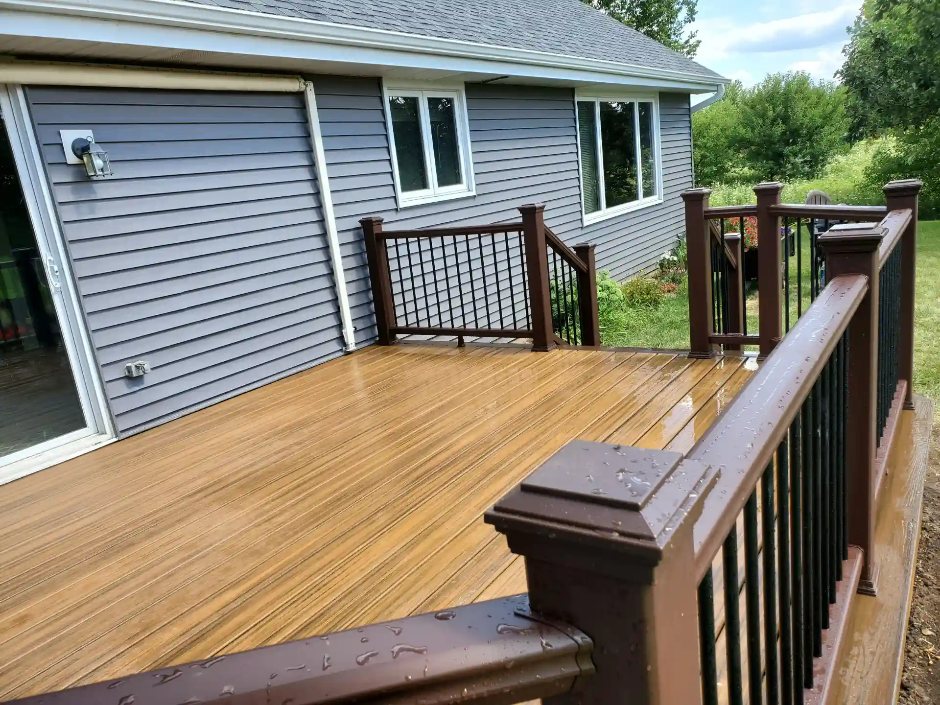 brown composite deck with black metal railings attached to a gray house