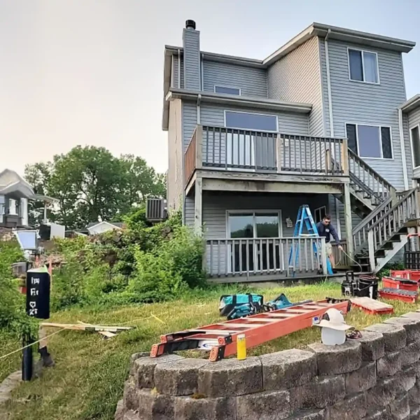 worker on ladder performing maintenance on a deck with tools and equipment nearby.