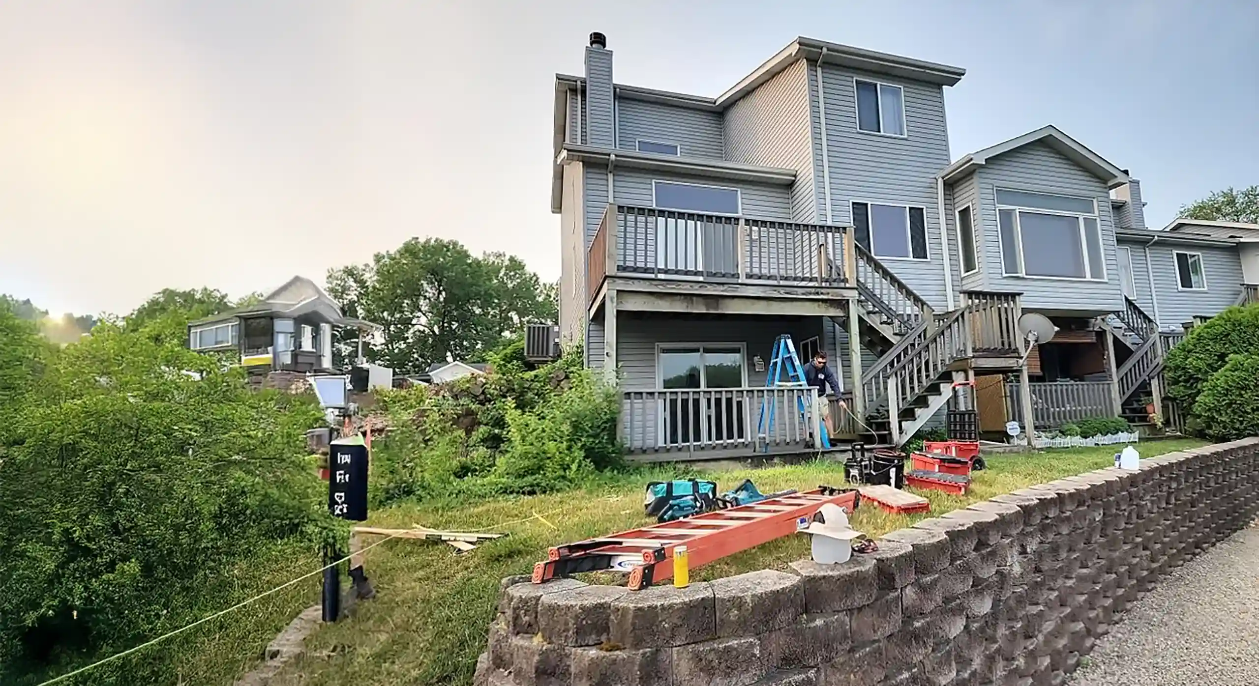 worker on ladder performing maintenance on a deck with tools and equipment nearby.