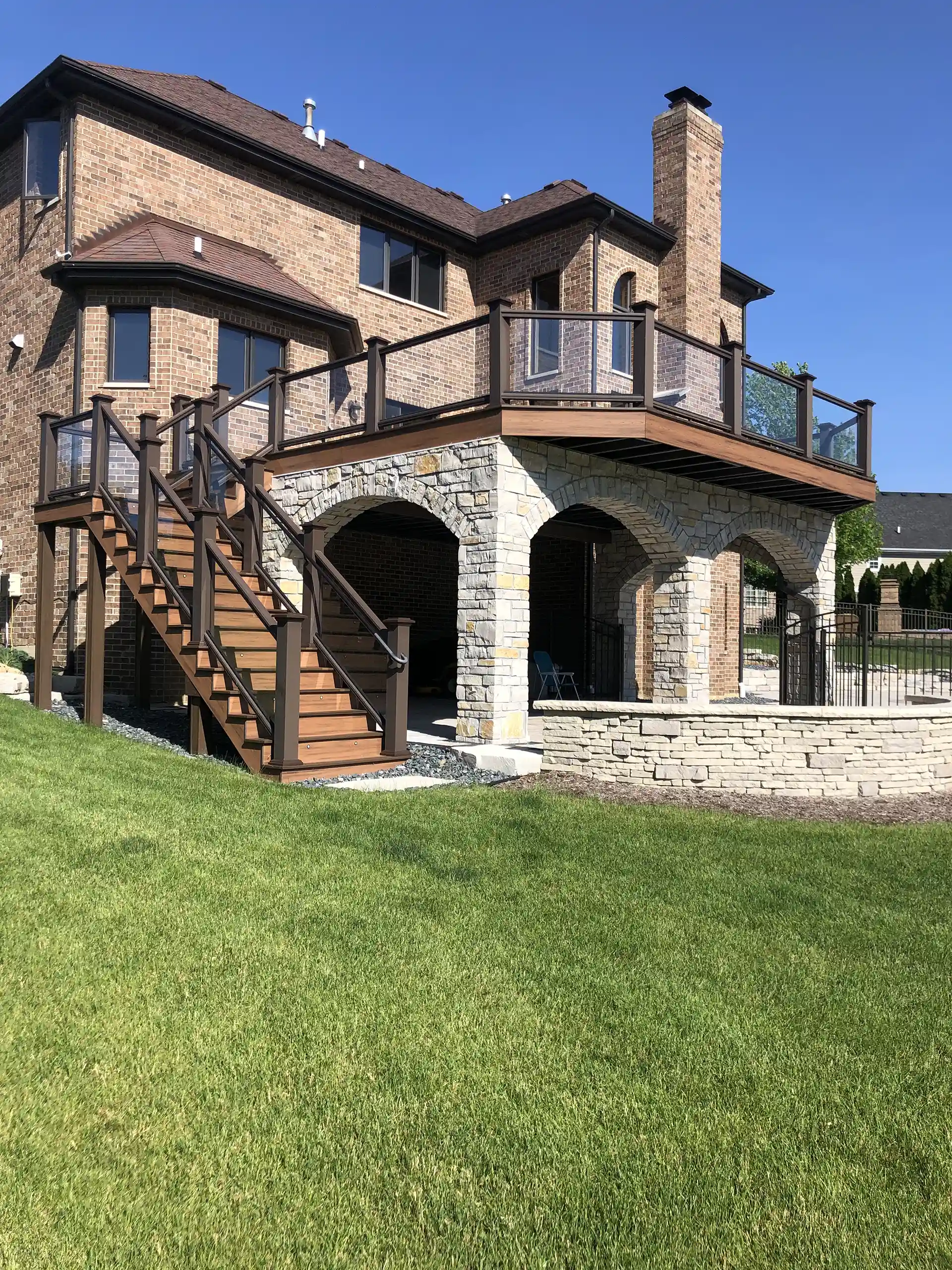 elevated deck with stone support columns and a wooden staircase, featuring glass railings