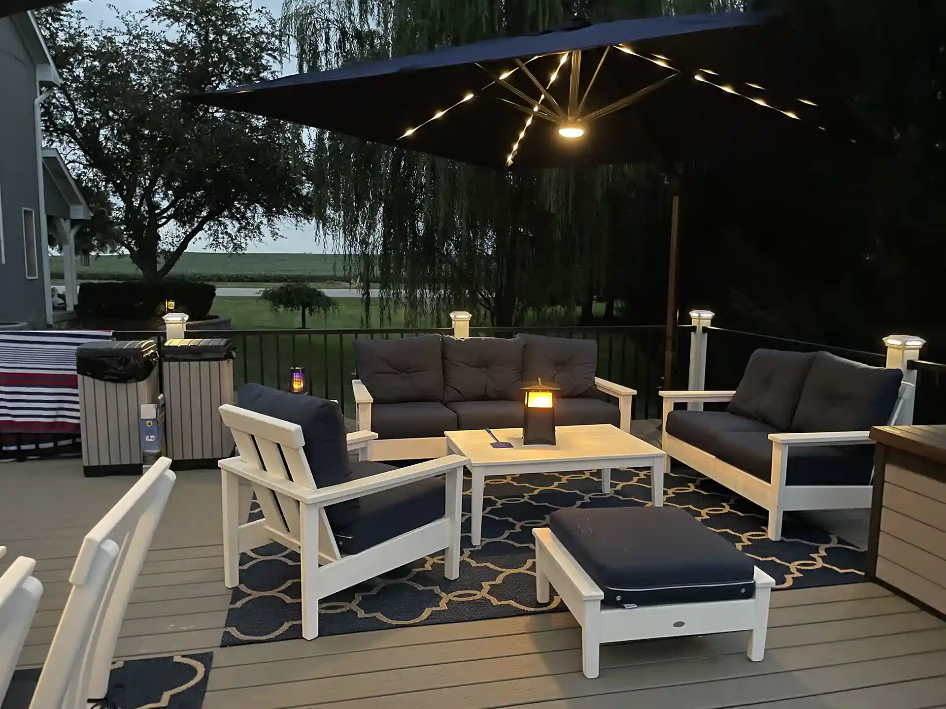 outdoor deck with cushioned seating, a large umbrella, and ambient lighting. 