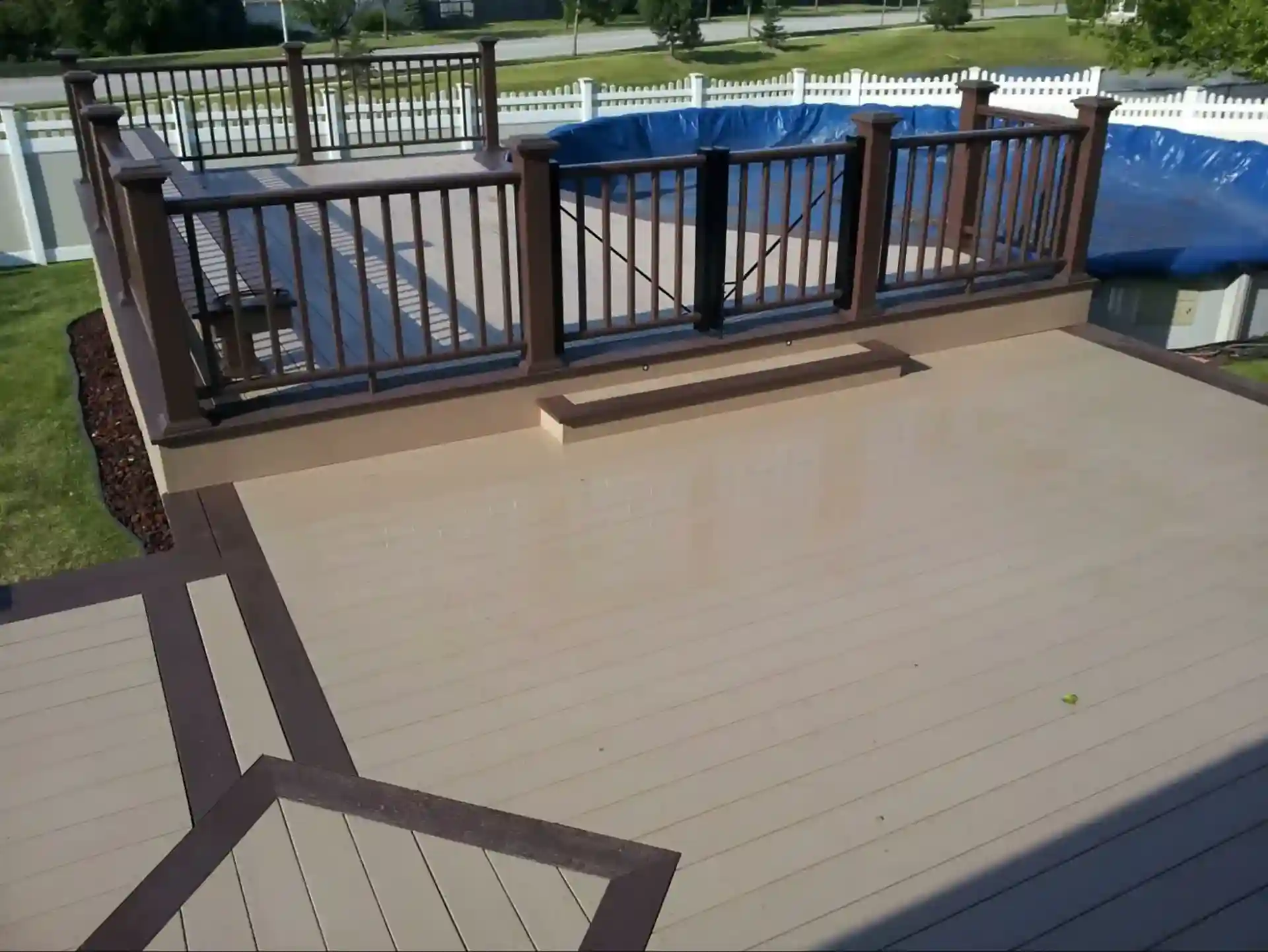 beige and brown multi-level composite pool deck with gated entry and decorative railing.