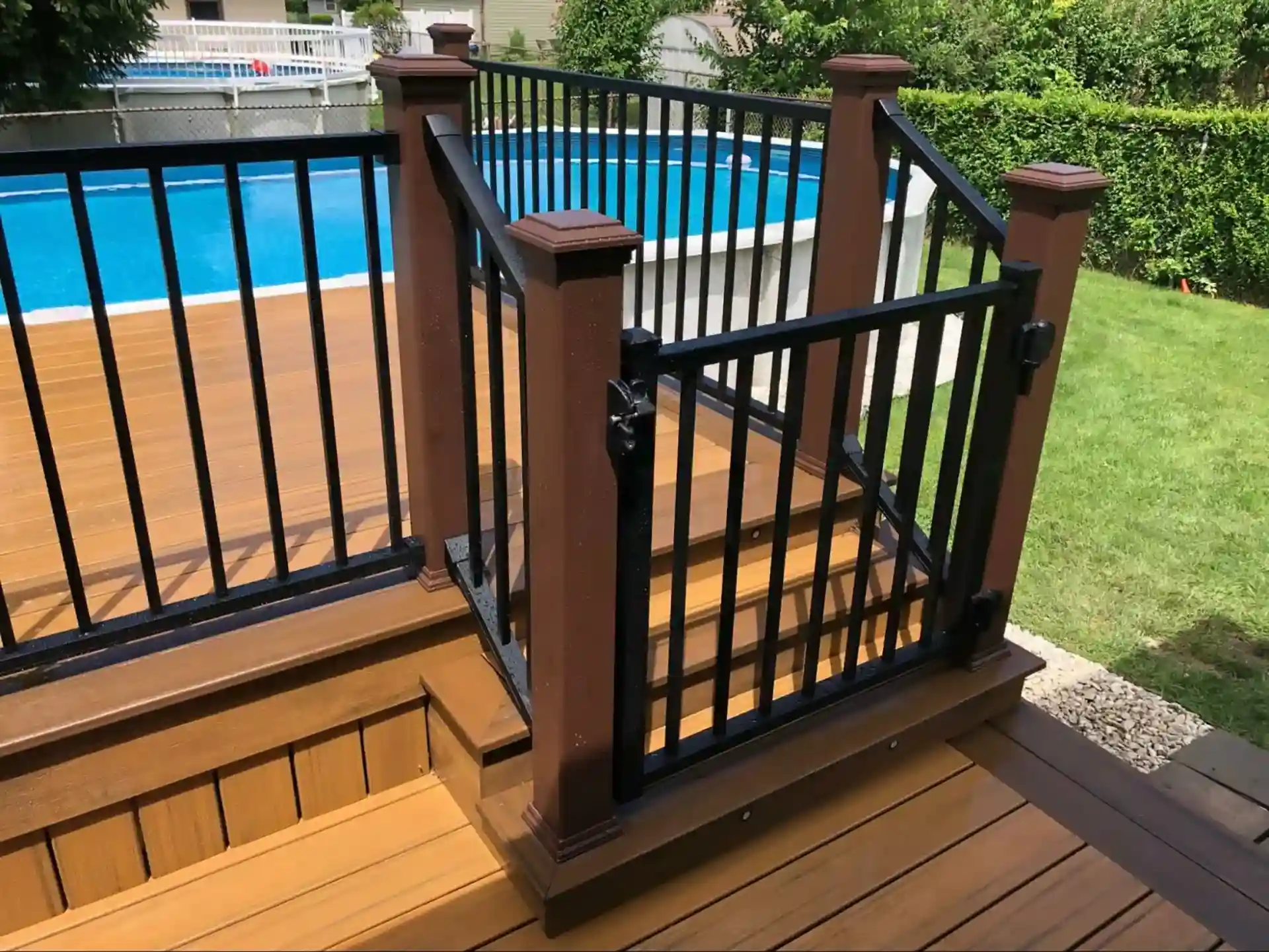 brown composite pool deck with black metal railing and a gated staircase leading to the yard