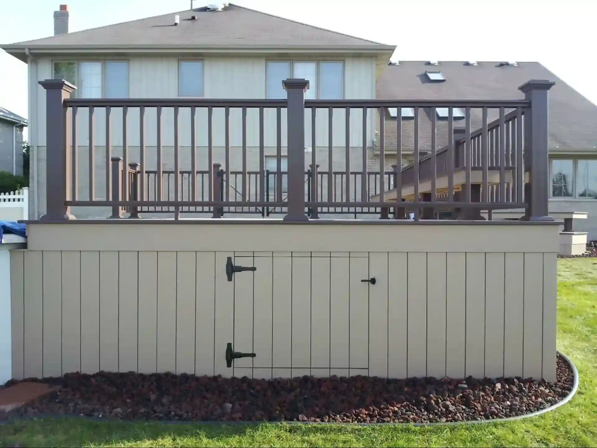 elevated beige and brown pool deck with storage access doors and decorative railing.