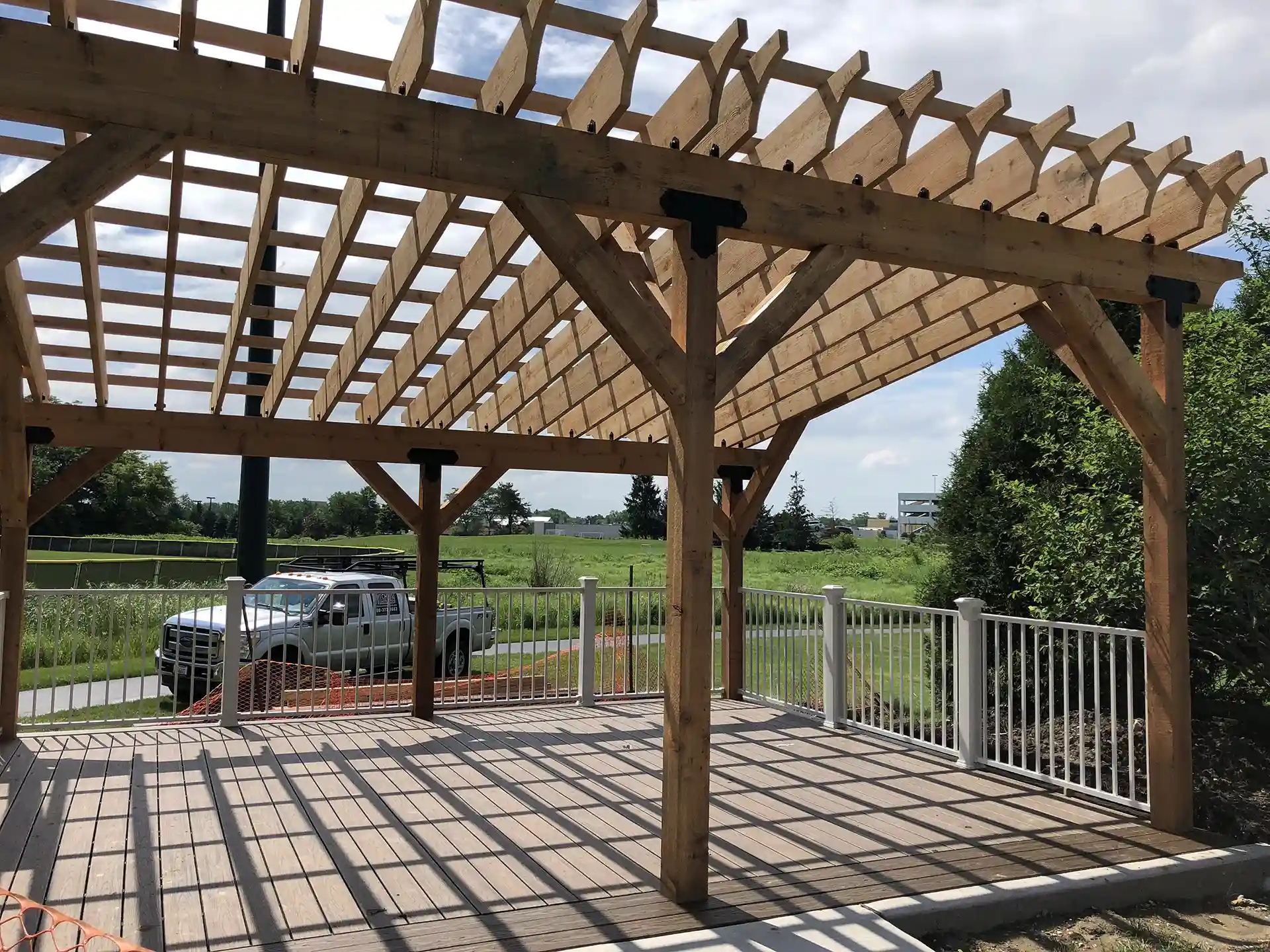 wooden pergola structure over a deck, with open slats casting shadows on the floor.
