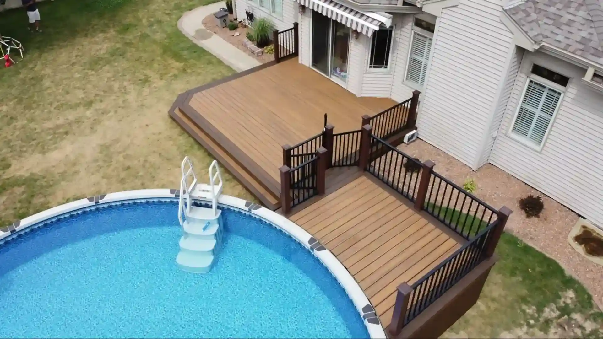 multi-level brown composite deck with black railings, connecting a home to an above-ground pool with stairs.