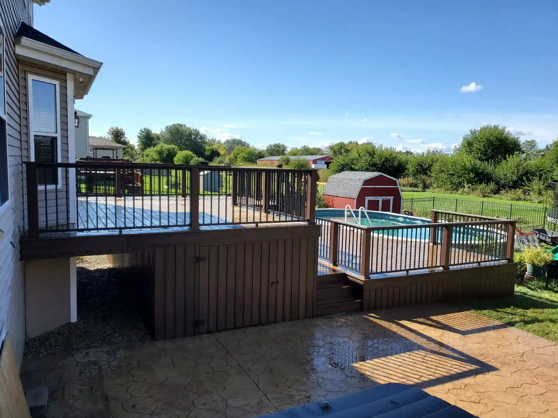 elevated wooden deck with black railing overlooking a pool and red shed