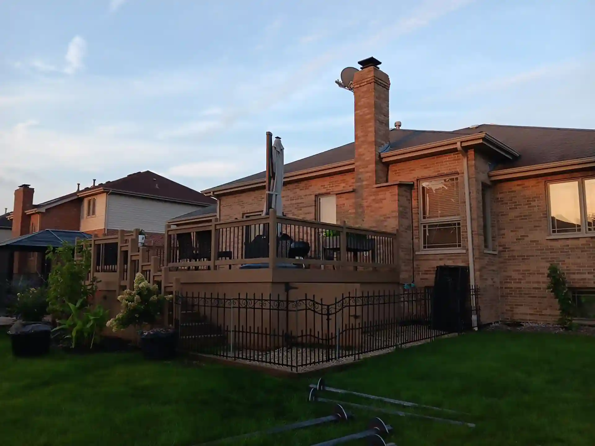 brick house with elevated deck and black picket fence at dusk