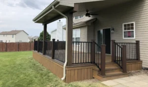 covered porch with a roof, wooden decking, black metal railings, and stairs leading to the yard. a ceiling fan is installed.