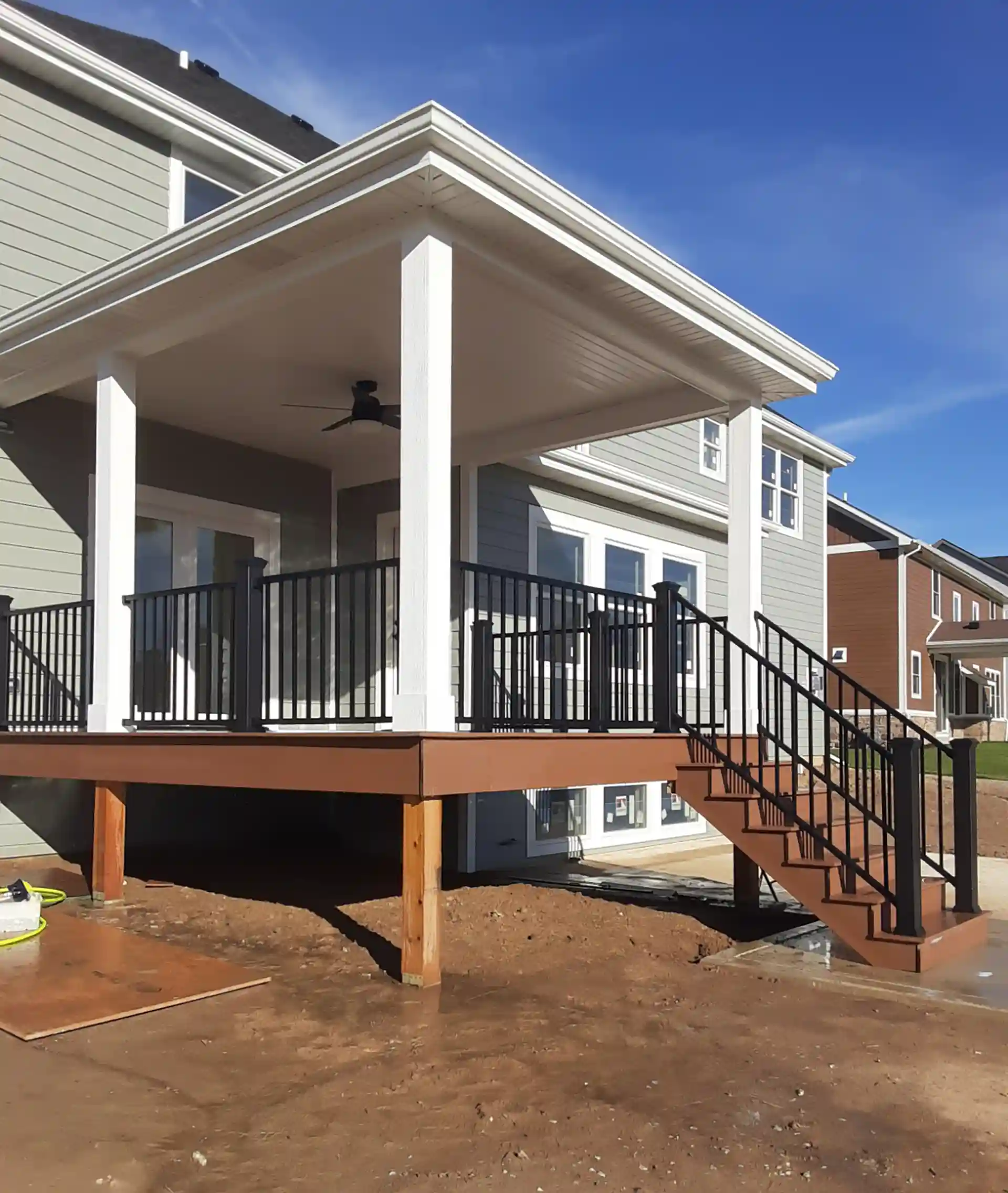 covered porch with a roof, wooden decking, and black metal railings. the porch is elevated with stairs leading down to the yard.
