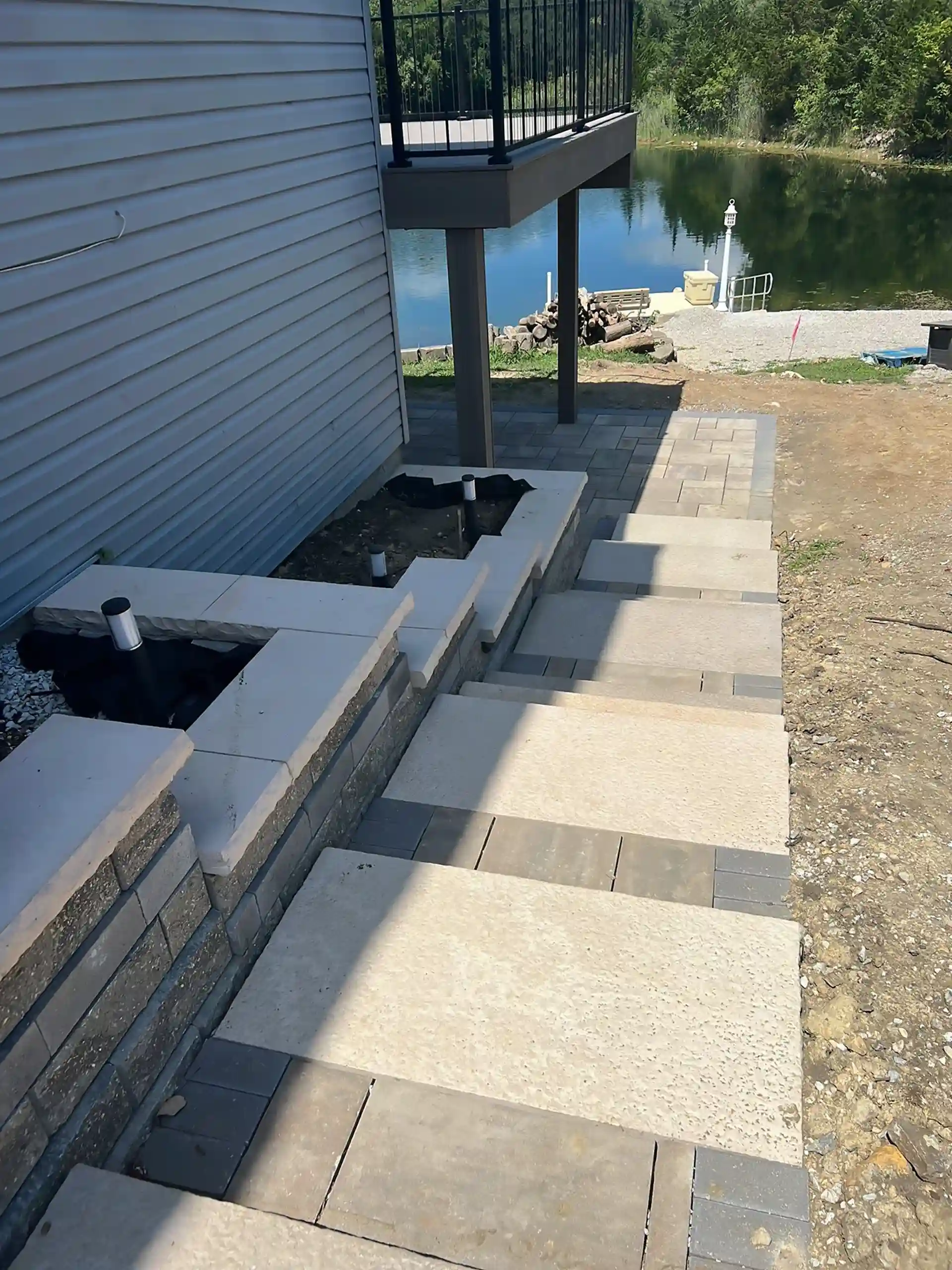 stone walkway with wide steps leading to a patio near a lake featuring retaining walls and modern pavers.
