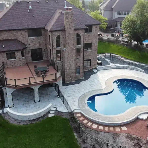 aerial view of an elevated deck with glass railing and a paver patio around a kidney-shaped pool.